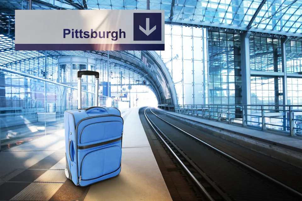 Blue suitcase sits on empty train platform with sign above labeled "Pittsburgh."
